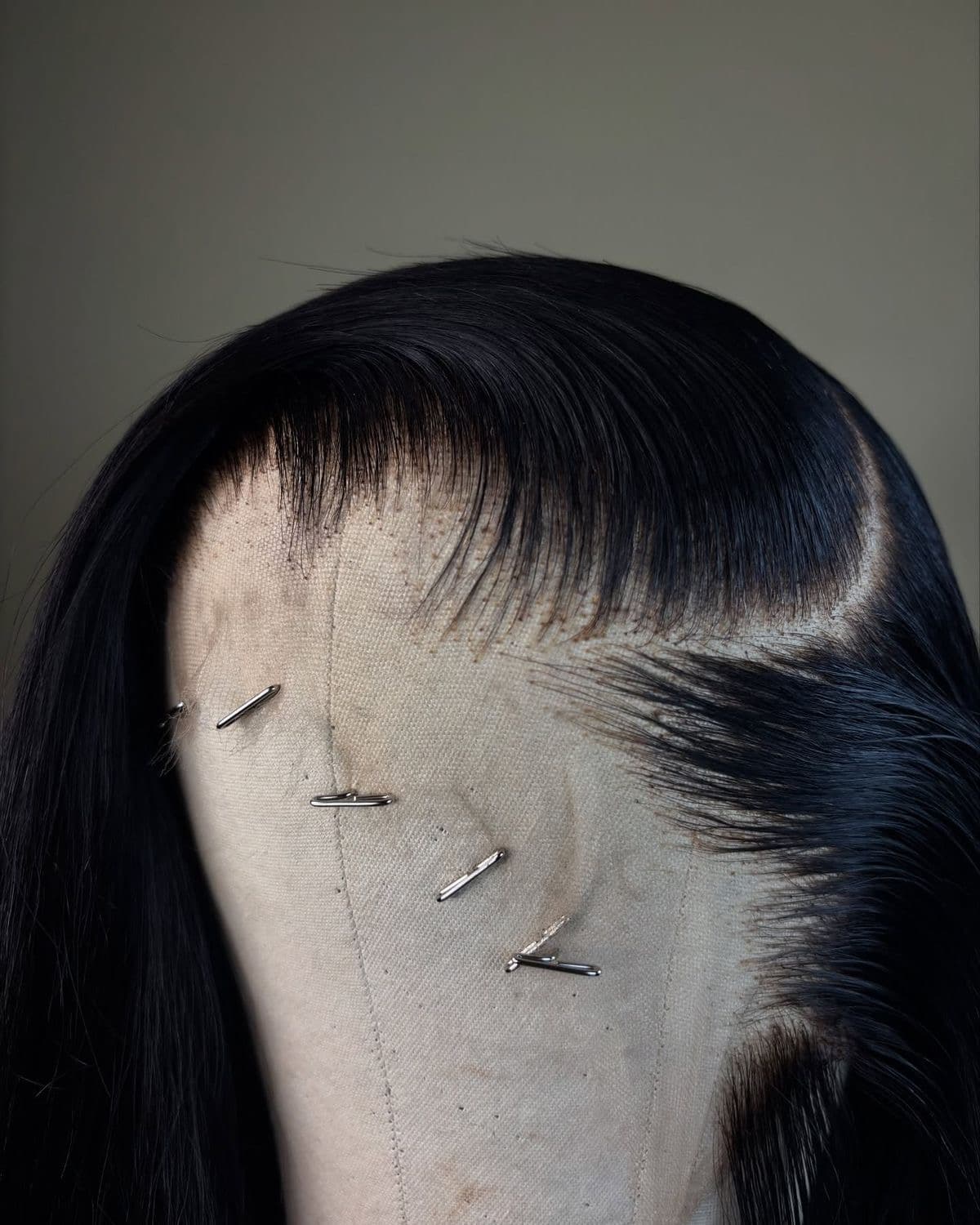Perruque en cheveux naturels lisses posée sur une tête de travail en toile, maintenue par des épingles